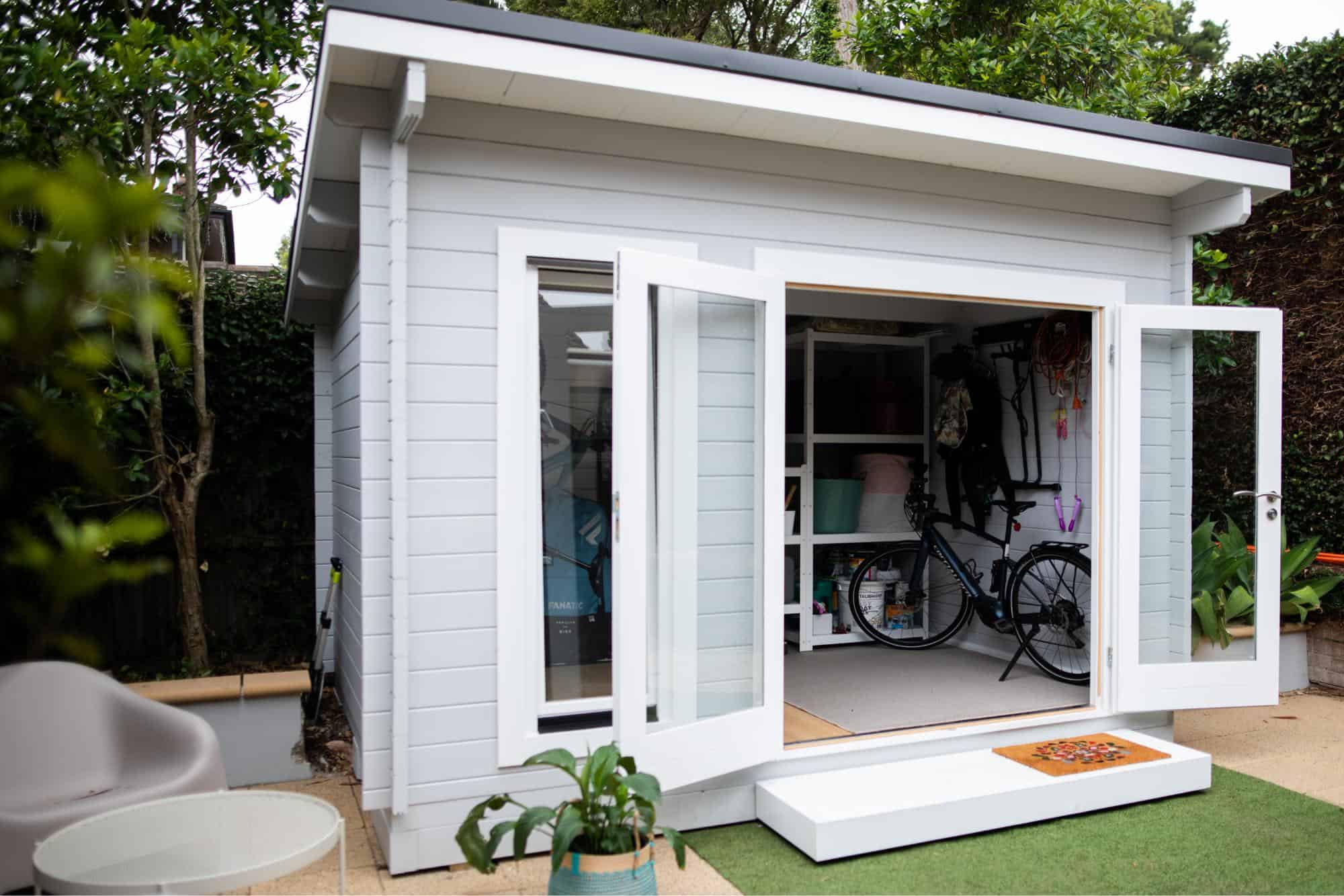 Garden shed with open doors and shelving and a bike inside.