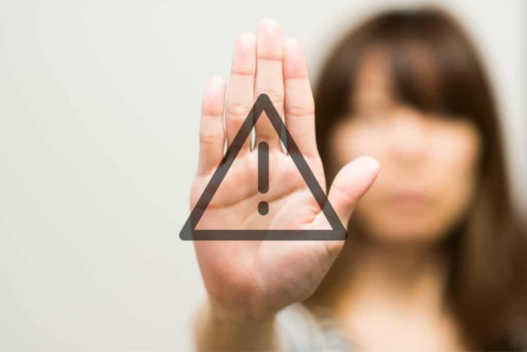 A blurred out image of a woman holding her hand up to the camera with an alert symbol in clear view.